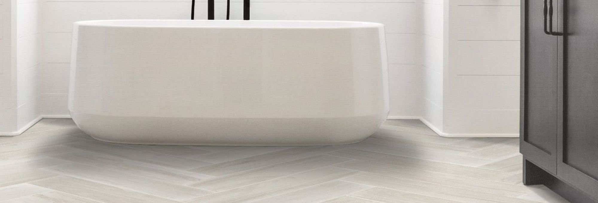 white bathtub in bathroom with white tile floor in herringbone style from Wholesale Flooring and Blinds in Casper, WY